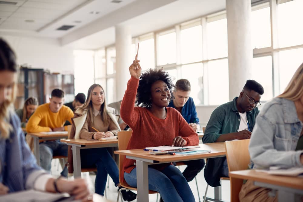 black girl, happy, raising hands, in class, sweater, white students, glasses, asking a question